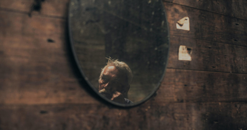 old man's face reflected in mirror