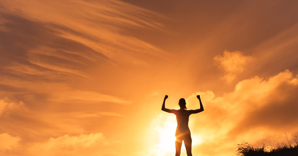 woman raising arms in front of sunset