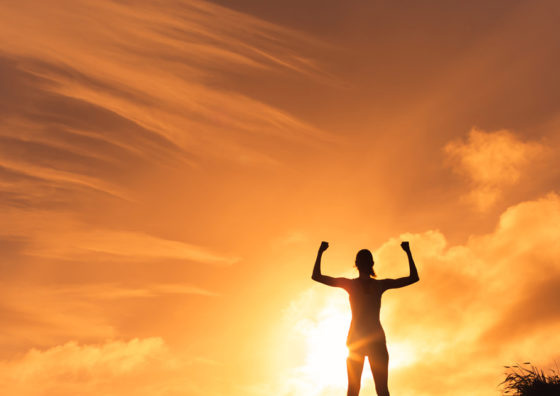 woman raising arms in front of sunset