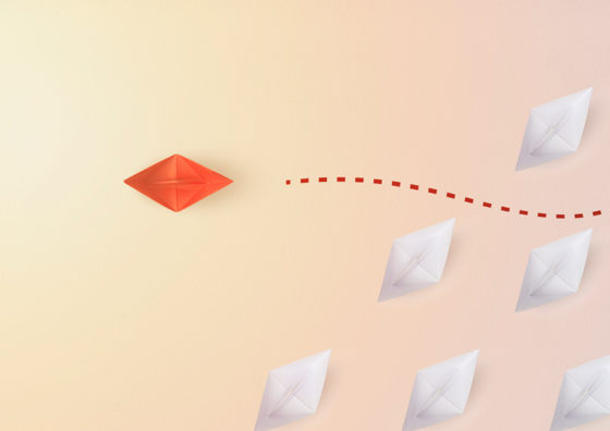 orange paper boat sailing away from fleet of white paper boats